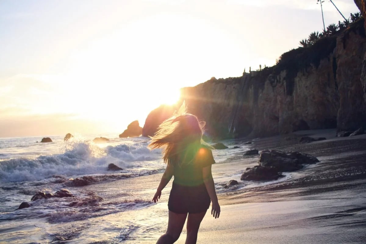 woman in green tank top and black shorts walking on beach during sunset