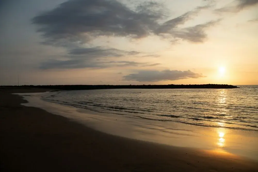 the sun is setting over the water at the beach