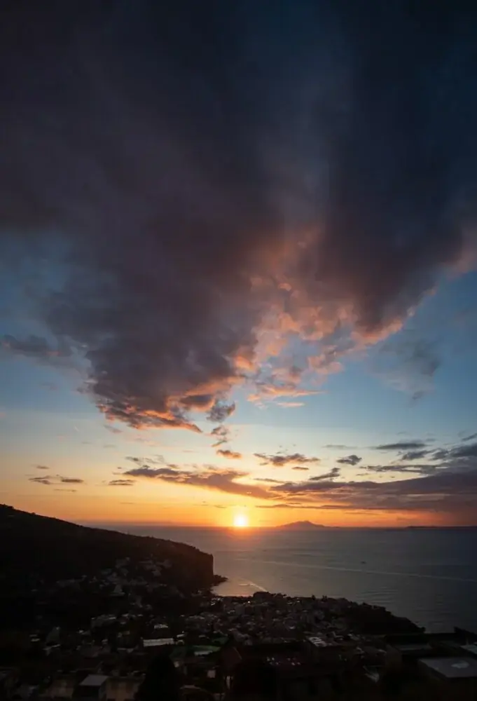 the sun is setting over a city and the ocean